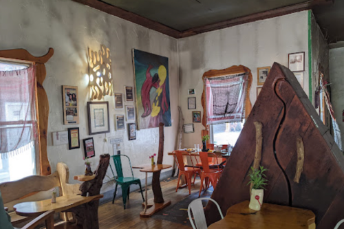 Cozy restaurant interior with unique wooden furniture, colorful artwork, and a warm, inviting atmosphere.