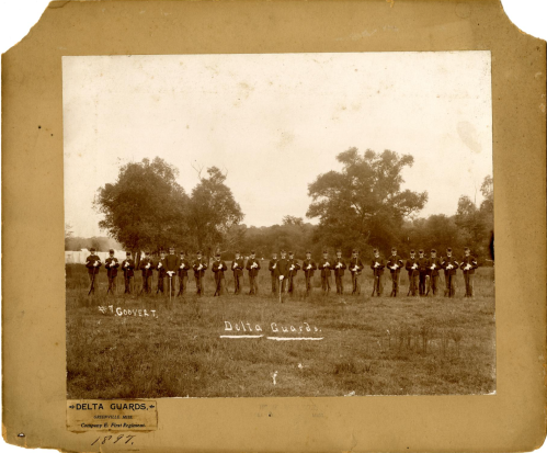 A historical black-and-white photo of the Delta Guards, a military group, standing in a field with trees in the background.