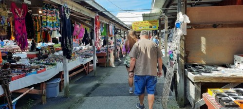 A bustling market scene with colorful stalls selling various goods and shoppers walking through the aisles.