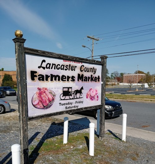 Sign for Lancaster County Farmers Market, featuring images of food and a horse-drawn carriage. Open Tuesday to Saturday.
