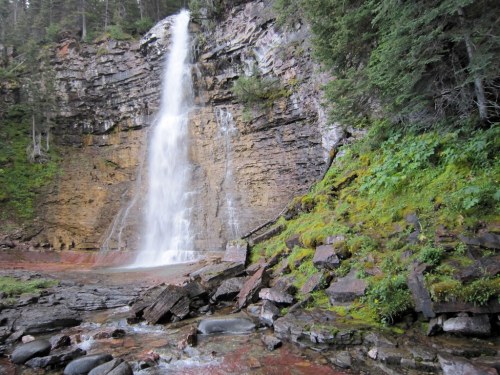 A serene waterfall cascades down a rocky cliff, surrounded by lush greenery and smooth stones.