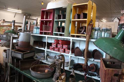 A vintage display of various antique items, including shelves, jars, and kitchen tools, in a rustic setting.