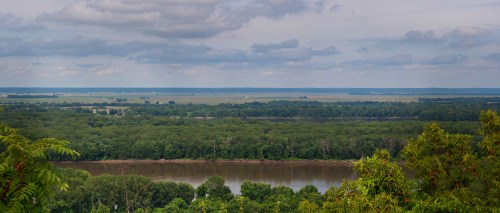 A panoramic view of a river winding through lush green forests under a cloudy sky.