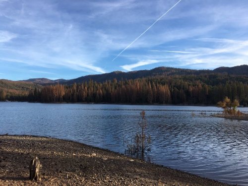 A serene lake surrounded by mountains, with a clear blue sky and scattered clouds reflecting on the water's surface.
