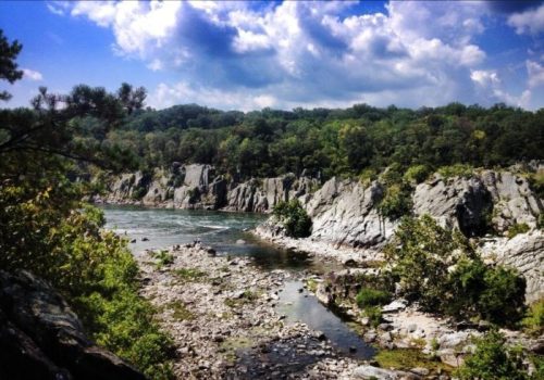 A scenic view of a river winding through rocky cliffs and lush greenery under a partly cloudy sky.
