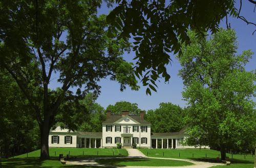 A large, historic white house surrounded by lush green trees and a clear blue sky.