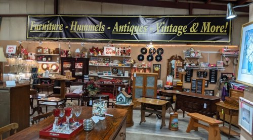 A vintage store interior featuring furniture, antiques, and collectibles, with a large promotional banner overhead.