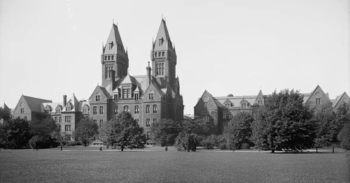 Historic building with twin towers, surrounded by trees and a grassy area, in black and white.