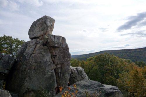 A large rock formation stands prominently against a backdrop of rolling hills and a cloudy sky.