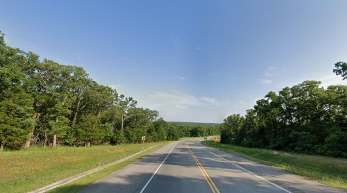 A winding road surrounded by lush green trees under a clear blue sky.