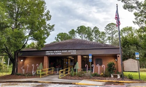 A U.S. Post Office building in Christmas, Florida, decorated with candy canes and surrounded by trees.