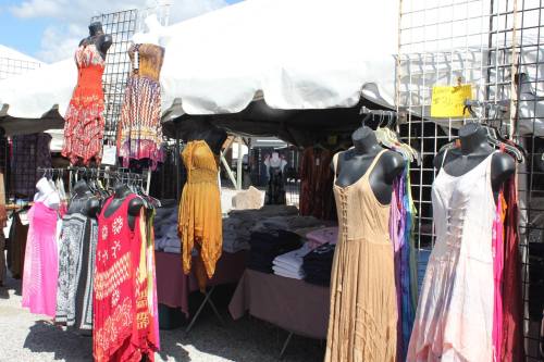 A vibrant outdoor market stall displaying colorful dresses on mannequins under a large tent.