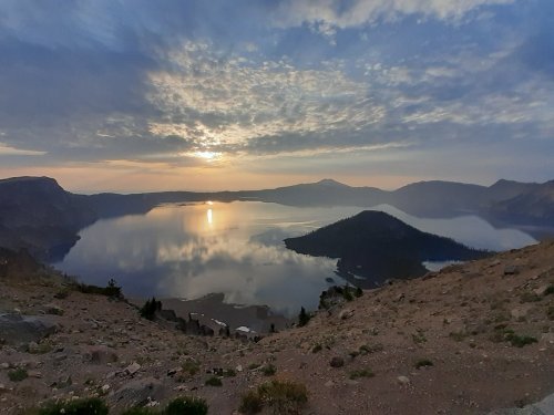 A serene lake at sunset, surrounded by mountains and a cloudy sky, reflecting the warm colors of the sun.