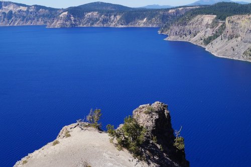 A stunning view of a deep blue lake surrounded by rocky cliffs and lush greenery under a clear sky.