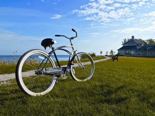 A bicycle parked on a grassy path near the ocean, with a house and a bench in the background under a blue sky.