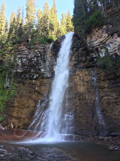 A stunning waterfall cascading down a rocky cliff, surrounded by lush green trees and a clear blue sky.