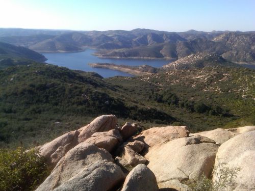 A scenic view of rolling hills and a lake surrounded by mountains under a clear blue sky.