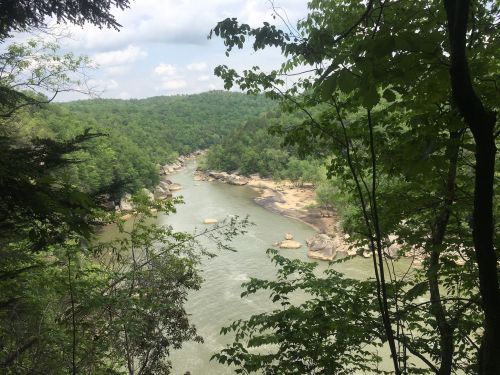 A serene river winds through lush green hills, framed by trees under a partly cloudy sky.