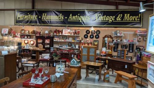 A store interior showcasing various furniture, antiques, and vintage items, with a large promotional banner overhead.
