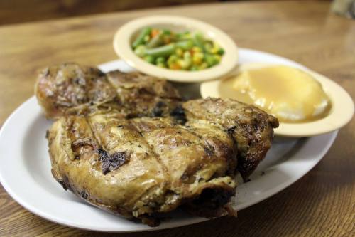 A plate of grilled chicken with sides of green beans, mixed vegetables, and a serving of mashed potatoes.