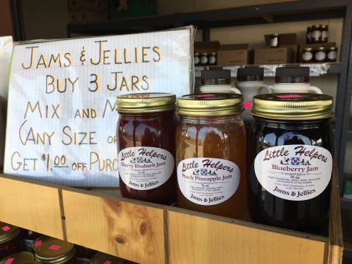 Three jars of jam on a wooden shelf, with a sign promoting a buy-three offer and a discount.