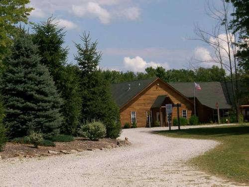 A gravel driveway leads to a wooden building surrounded by trees and greenery under a partly cloudy sky.