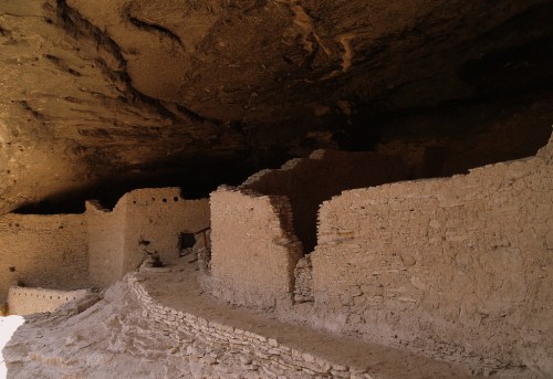 Ancient cliff dwellings made of stone and adobe, nestled under a rocky overhang.