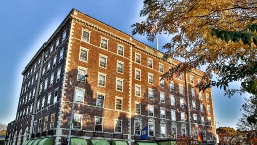 Historic brick building with large windows, an American flag, and autumn foliage in the foreground.