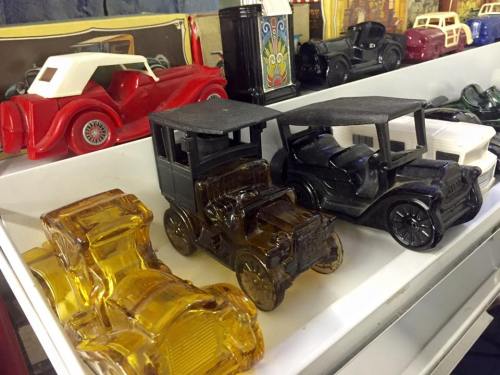 A display of vintage toy cars in various colors, including yellow, black, and clear, arranged on a shelf.