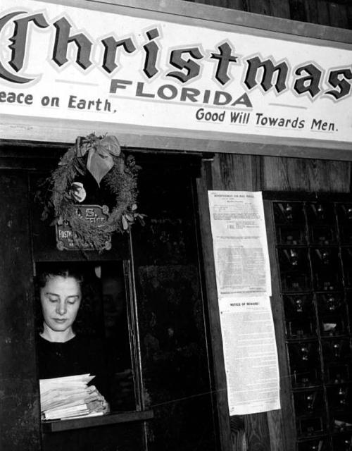 A young woman stands at a window in Christmas, Florida, surrounded by holiday decorations and mailboxes.