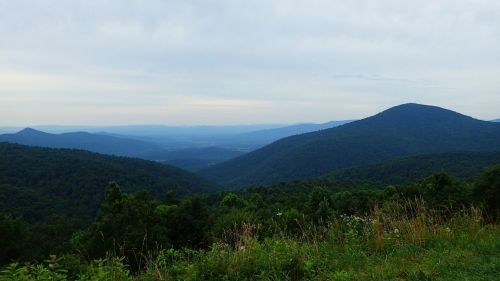 A panoramic view of rolling green mountains under a cloudy sky, with valleys stretching into the distance.