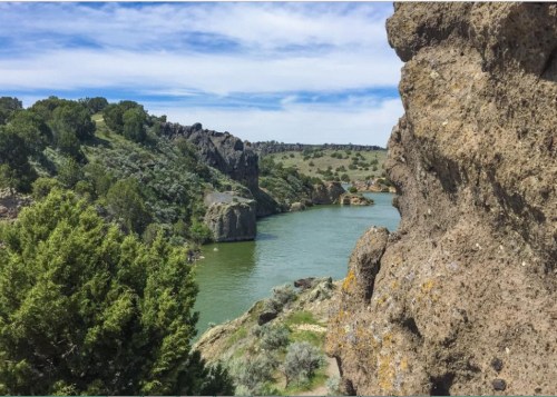 Scenic view of a river winding through rocky terrain and lush greenery under a blue sky with scattered clouds.