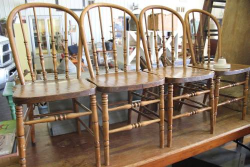 Four wooden chairs with spindled backs lined up on a table in a rustic setting.