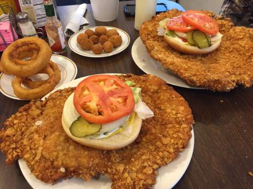 Two large fried chicken sandwiches with lettuce, tomato, and pickles on buns, served with onion rings and fried snacks.