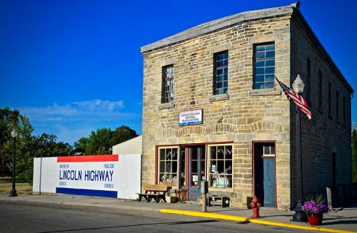 Historic stone building with an American flag, featuring a sign for the Lincoln Highway and benches outside.