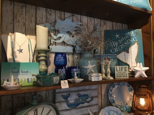 A wooden shelf displays coastal-themed decor, including candles, starfish, and signs in shades of blue and white.