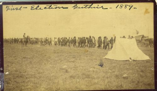 Historic photo of a large group of people at the first election in Guthrie, 1889, with tents and a horse in the background.