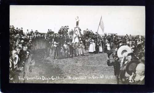 A historic gathering at a monument during the first Decoration Day, with a crowd in period clothing and flags.