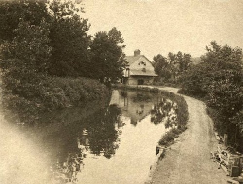 A serene, vintage scene of a winding river beside a house, surrounded by trees and lush greenery.