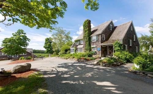 A charming, rustic house with a stone chimney, surrounded by greenery and a gravel driveway under a blue sky.