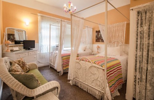 A cozy bedroom with two canopy beds, colorful striped bedding, a chandelier, and a wicker seating area.