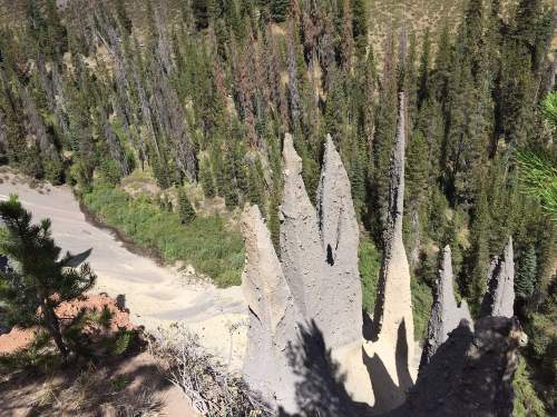 Aerial view of tall, spire-like rock formations surrounded by dense green forest and a winding river below.