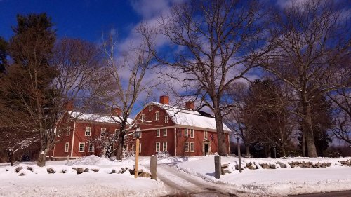 A red brick house surrounded by snow, with bare trees and a blue sky in the background.