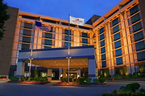 Exterior view of a well-lit hotel entrance at dusk, featuring American and hotel flags, surrounded by landscaped flowers.
