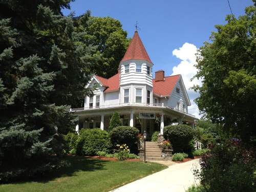 A charming Victorian-style house with a turret, surrounded by lush greenery and a clear blue sky.