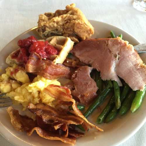 A plate of food featuring fried chicken, bacon, scrambled eggs, green beans, and a red sauce.