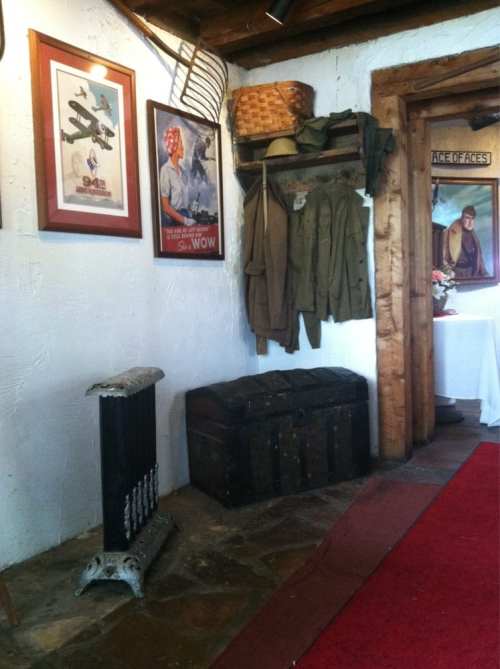 A cozy room corner featuring vintage military uniforms, posters, a wooden chest, and a decorative radiator.