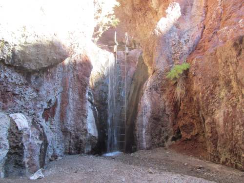 A waterfall cascading down rocky cliffs into a small, dry area below, surrounded by rugged terrain.