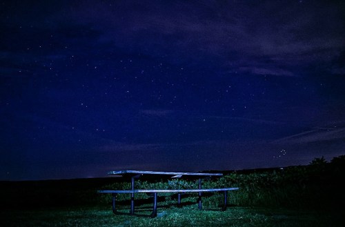 A picnic table silhouetted against a starry night sky with dark clouds.