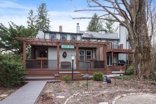 A charming two-story house with a wooden porch, surrounded by trees and landscaped gardens.